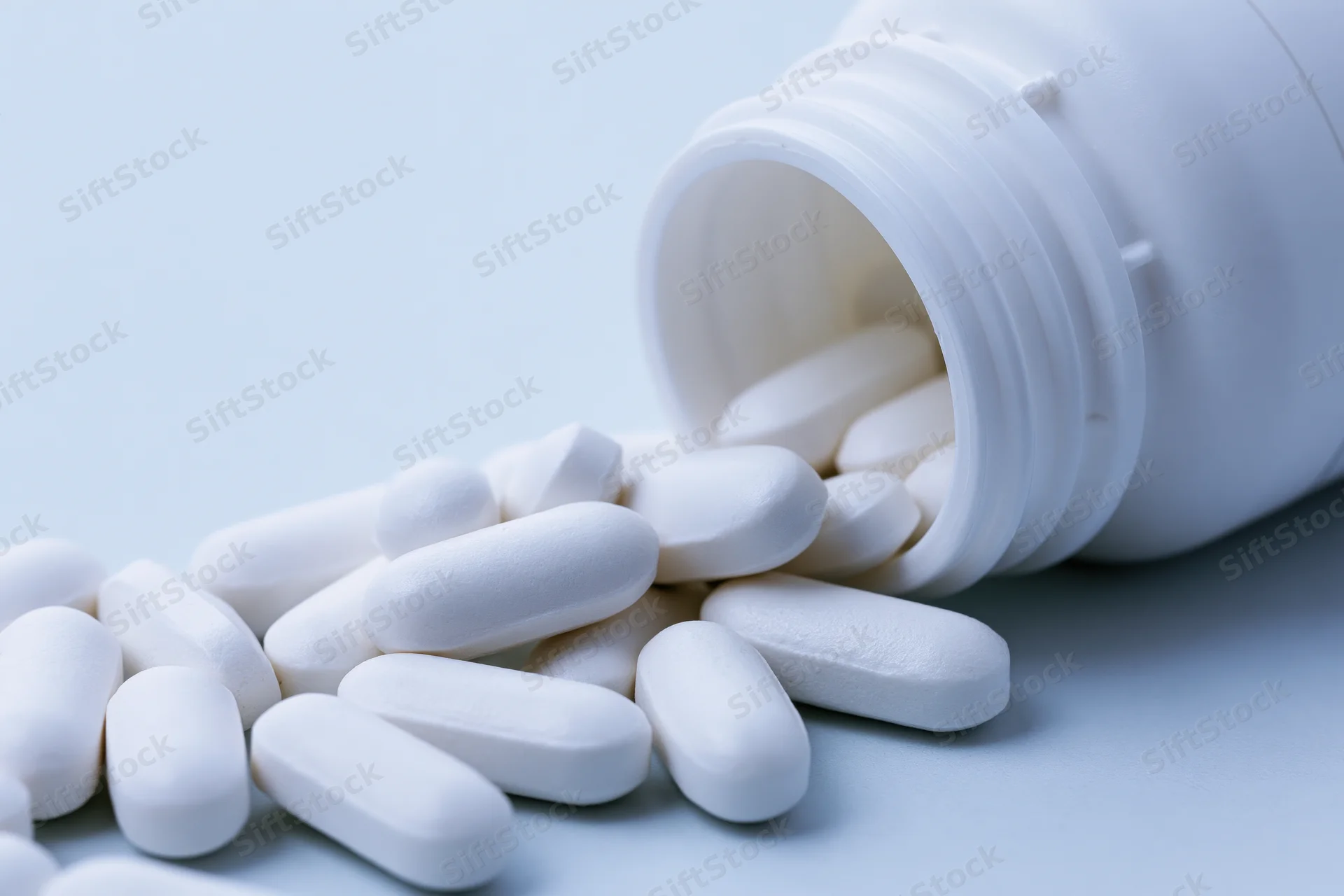 White oval pills spilling from an overturned plastic bottle on a light surface
