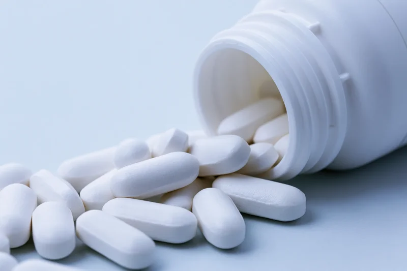 White oval pills spilling from an overturned plastic bottle on a light surface