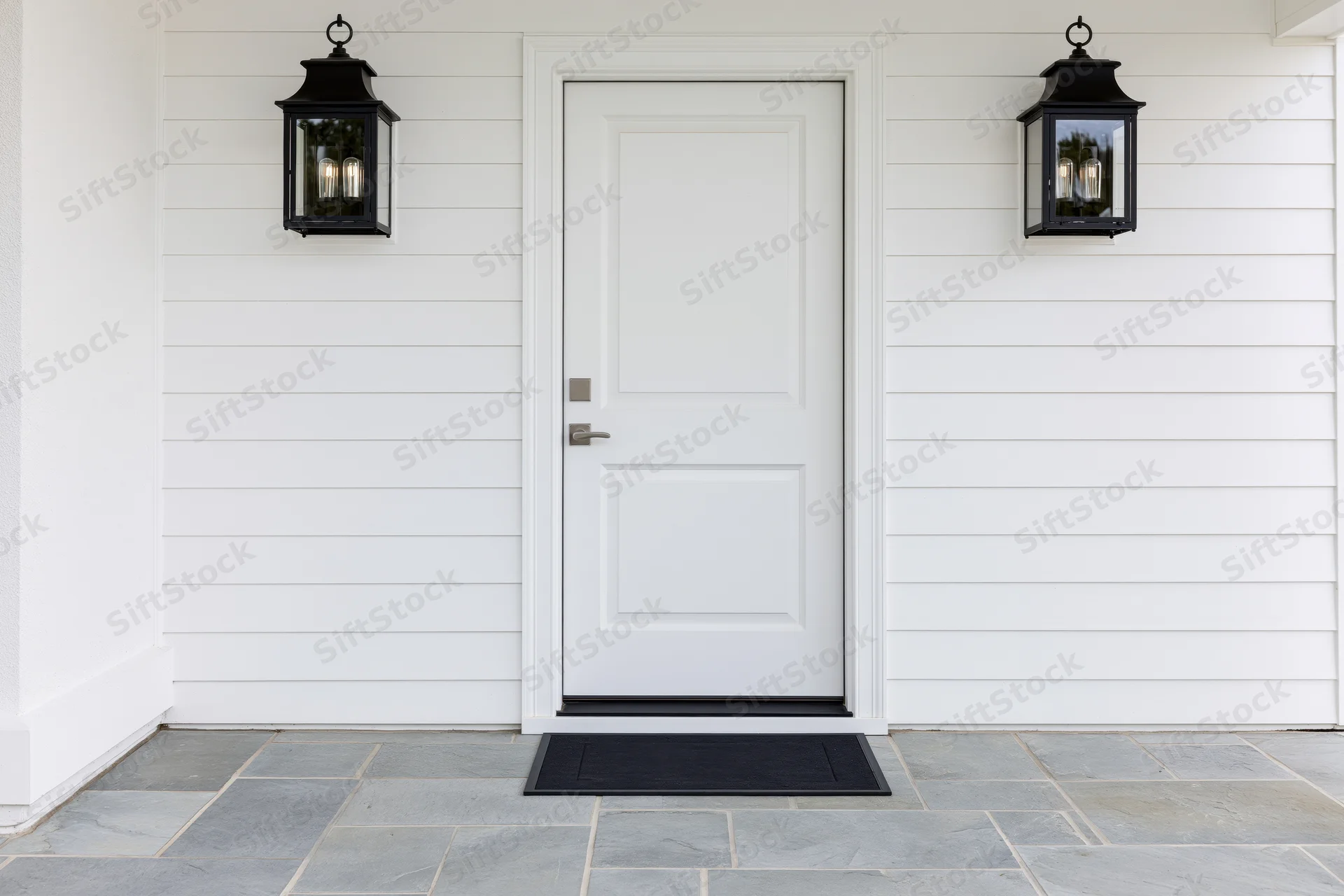 White raised-panel front door centered on a house exterior with black lantern lights and stone flooring