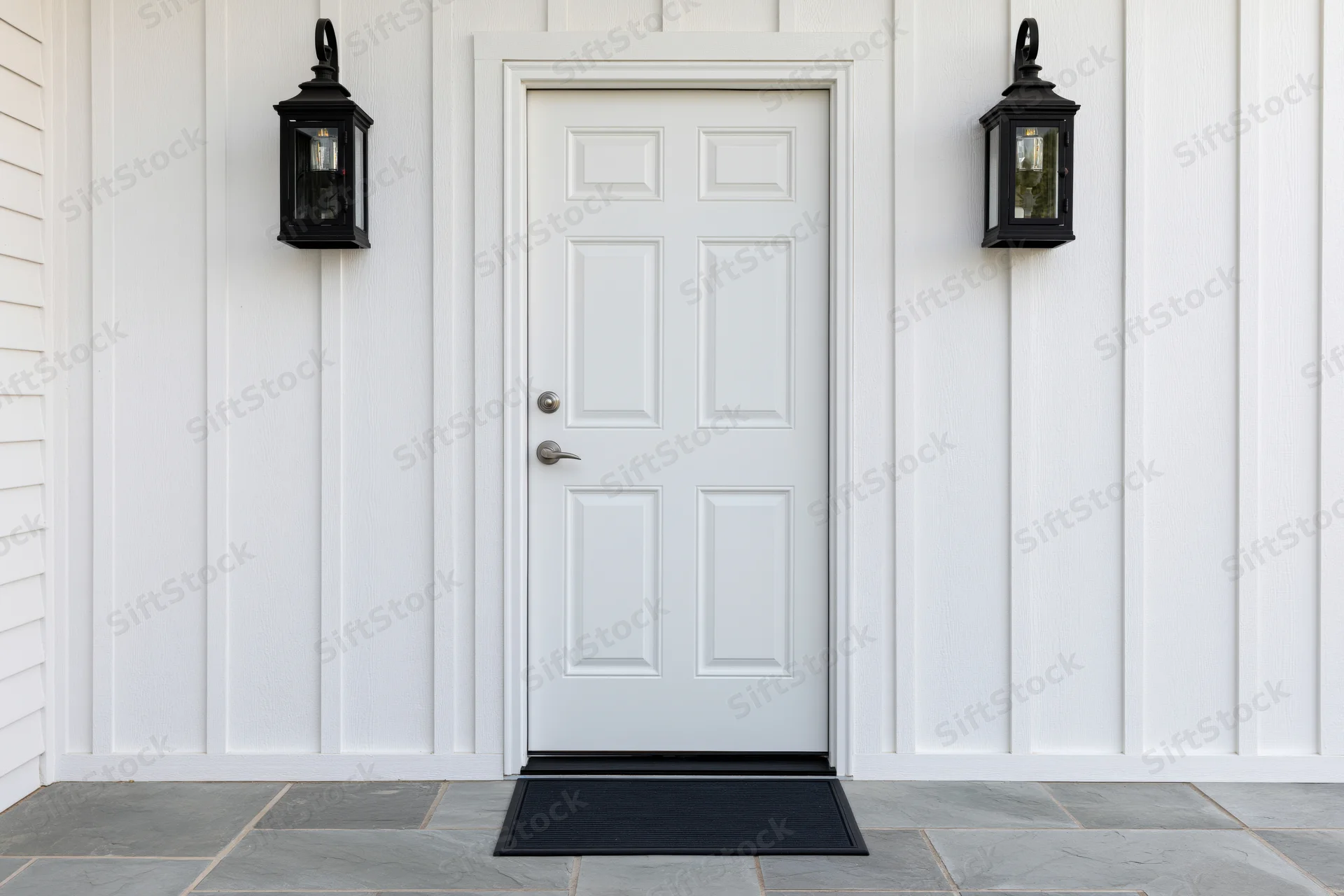 White raised-panel front door centered between black lanterns on a vinyl-siding house exterior