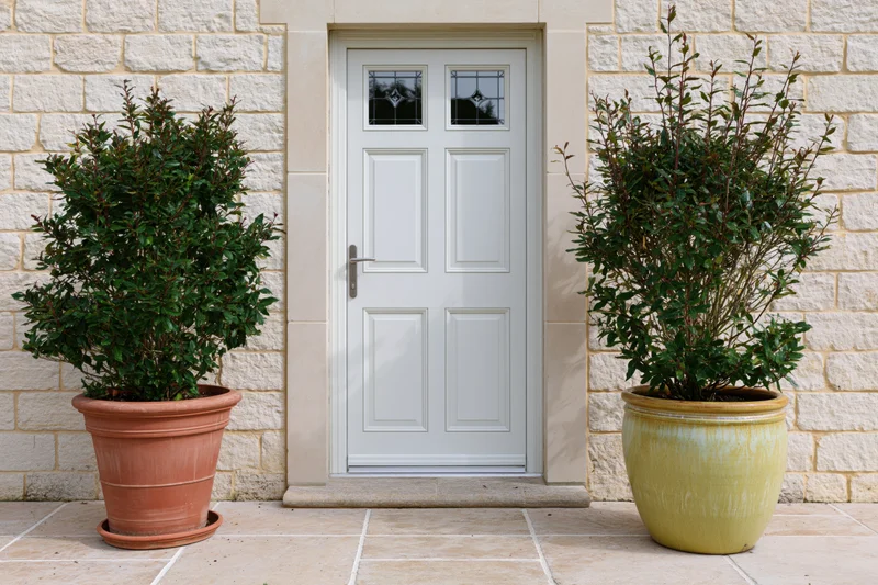 White paneled front door with decorative glass inserts flanked by potted plants on a stone porch