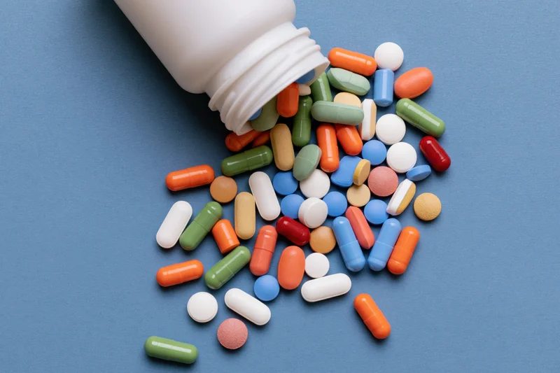Assorted pills spilling from a white plastic bottle onto a blue surface