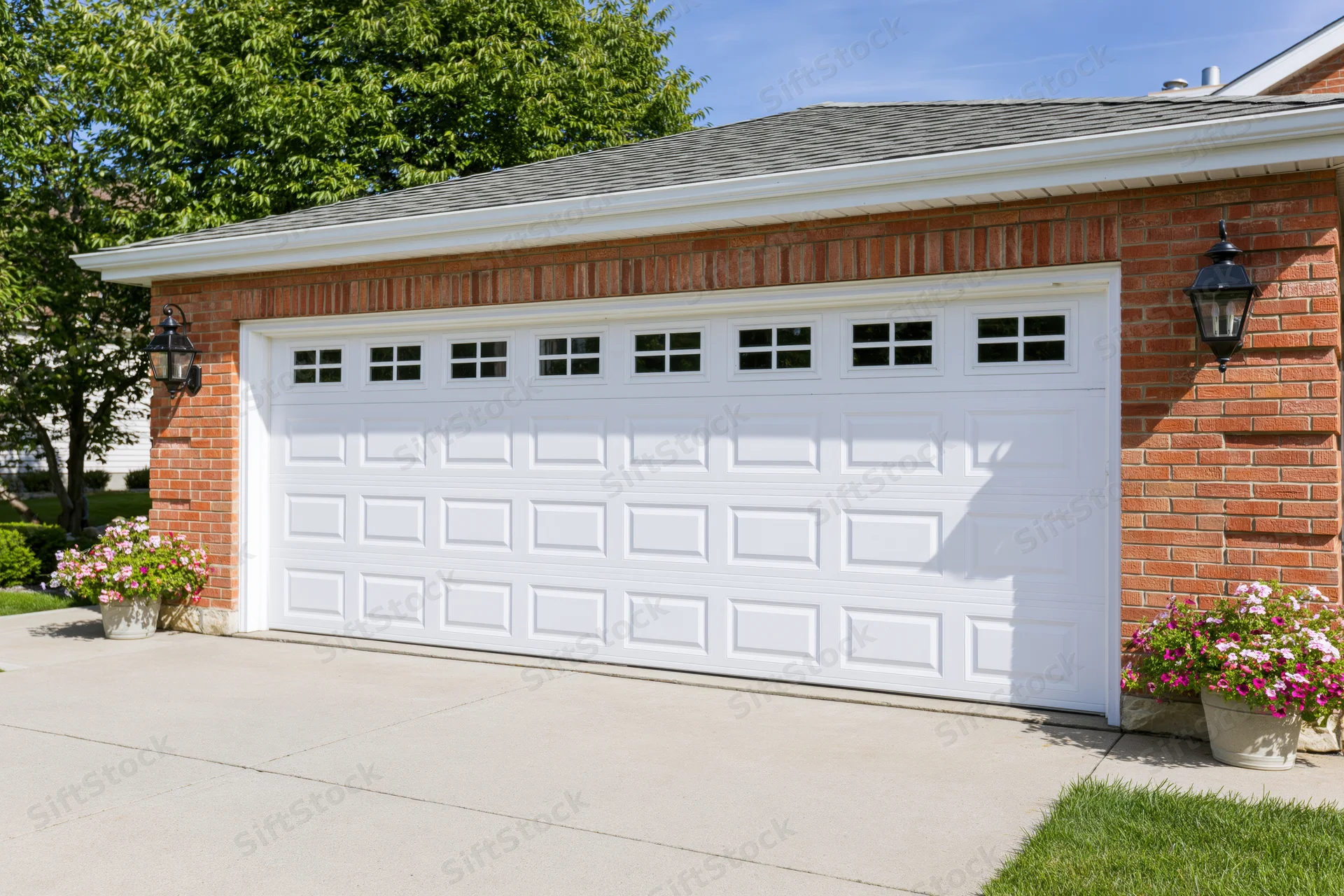 White raised-panel double garage door on brick house with flower pots and driveway