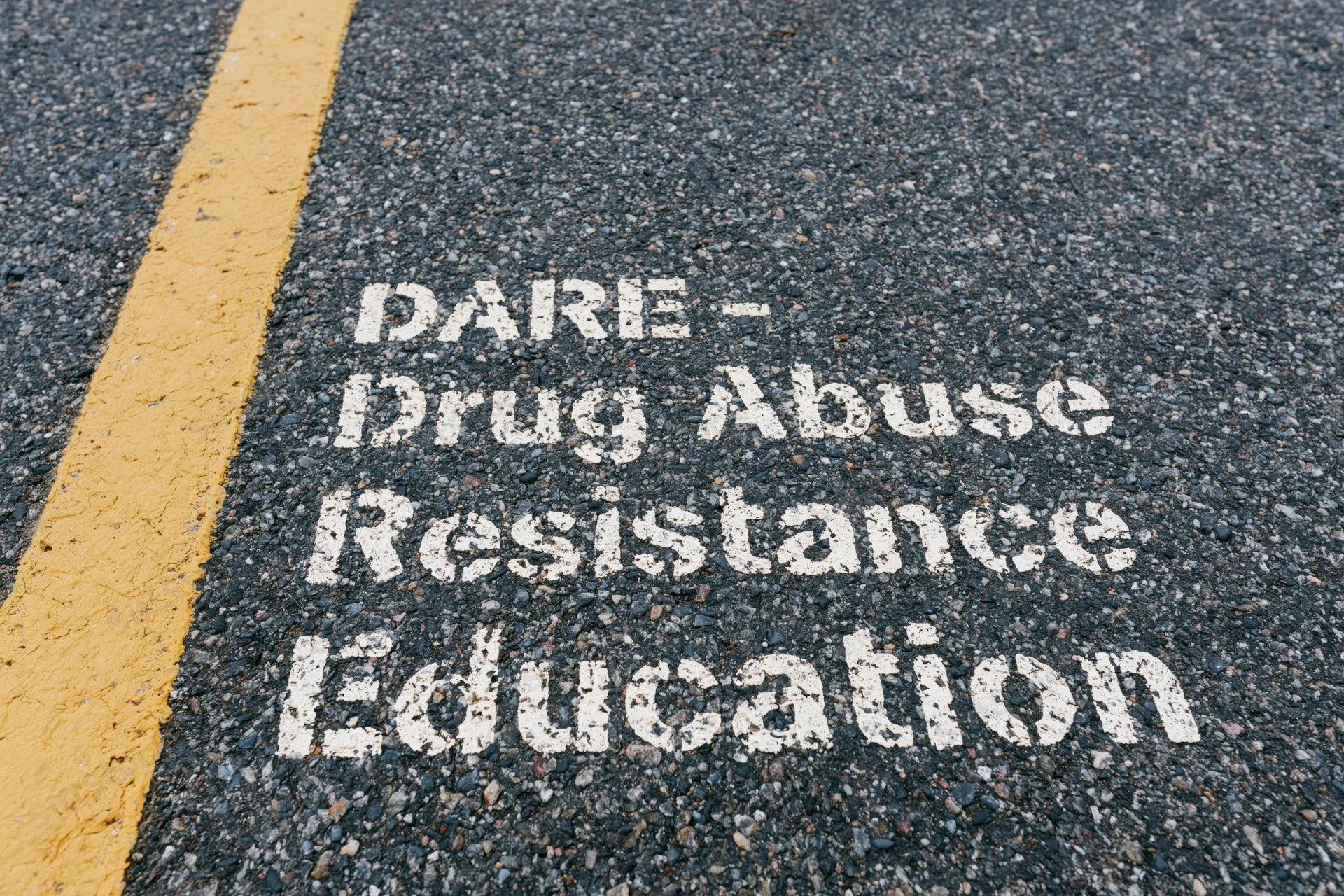 White stenciled dare acronym painted on dark asphalt road next to yellow line
