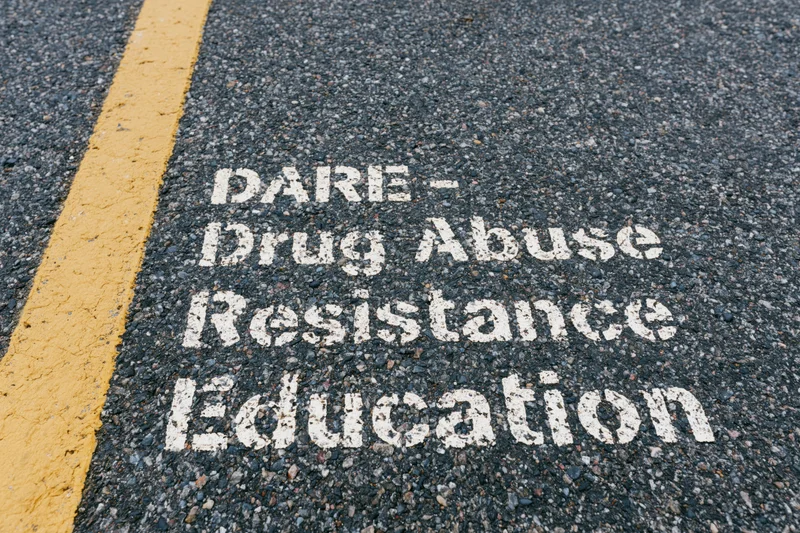 White stenciled dare acronym painted on dark asphalt road next to yellow line