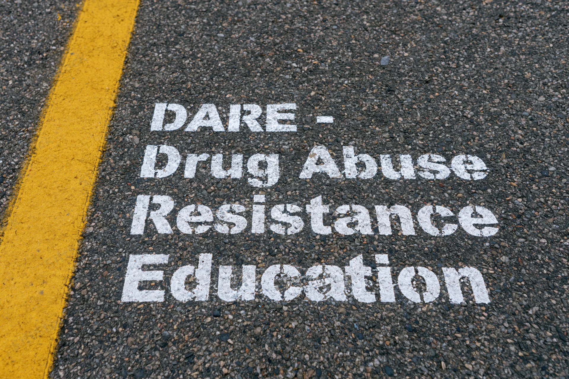 White stenciled dare text painted on dark asphalt road surface next to yellow line