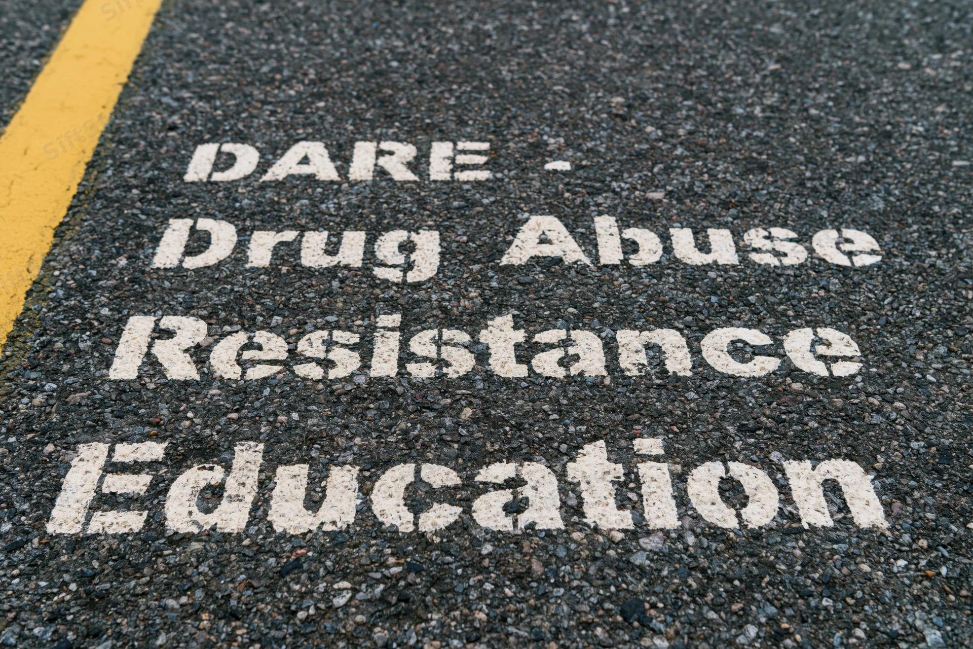 White stenciled dare acronym painted on dark asphalt pavement near yellow road line