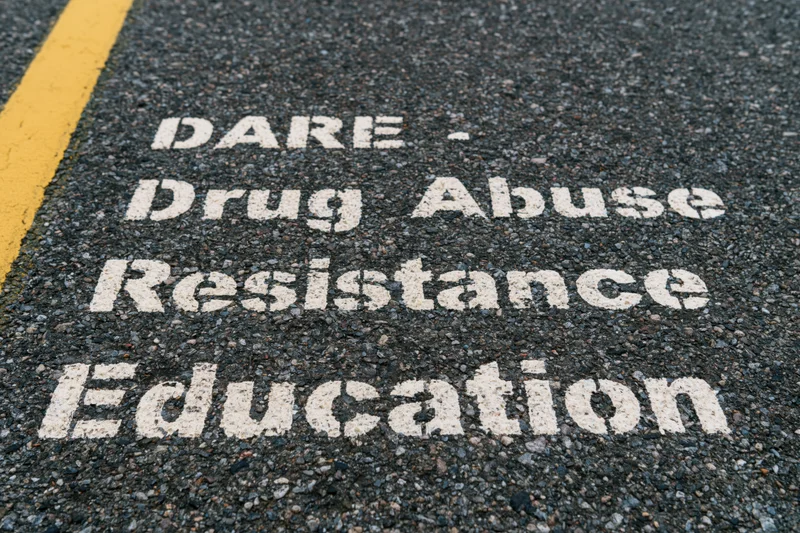 White stenciled dare acronym painted on dark asphalt pavement near yellow road line
