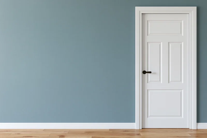 White three-panel interior door with dark lever handle against blue wall in empty room