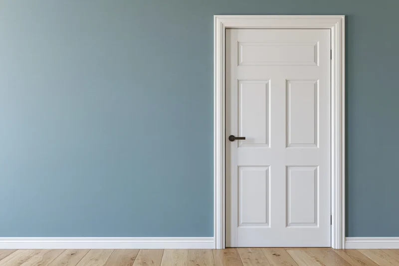 White panel door with dark lever handle closed against blue wall in empty room
