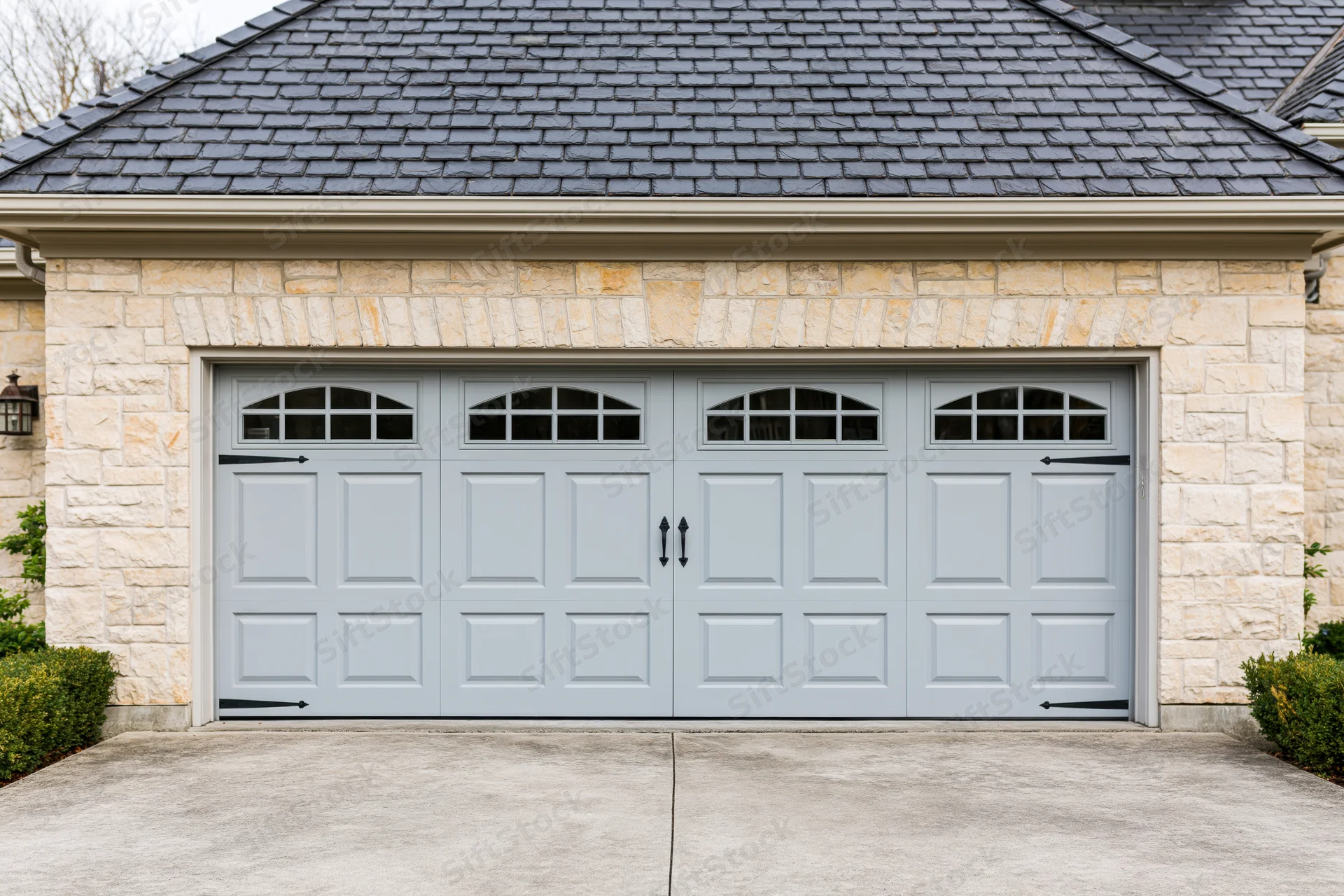Double garage door with decorative panels and arched windows on a stone facade house