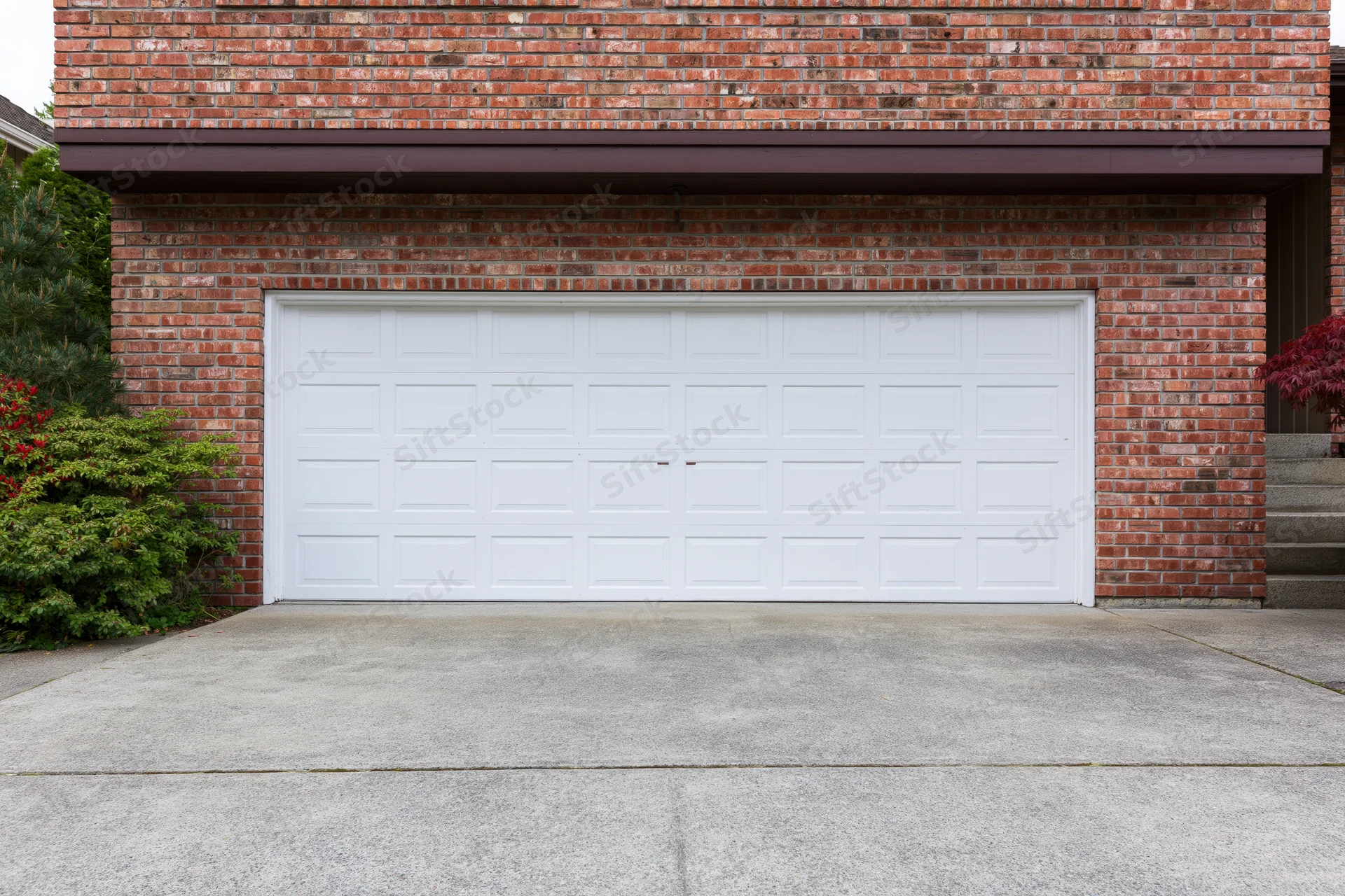 White two-car garage door on red brick residential house exterior with concrete driveway