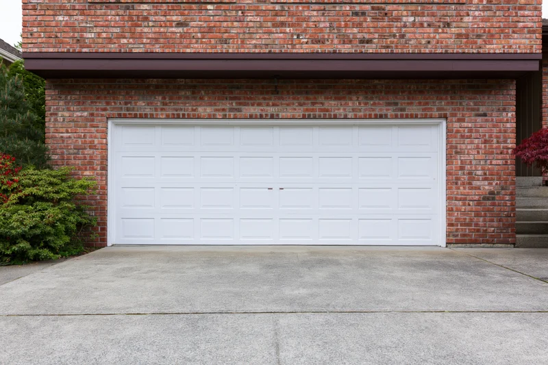 White two-car garage door on red brick residential house exterior with concrete driveway