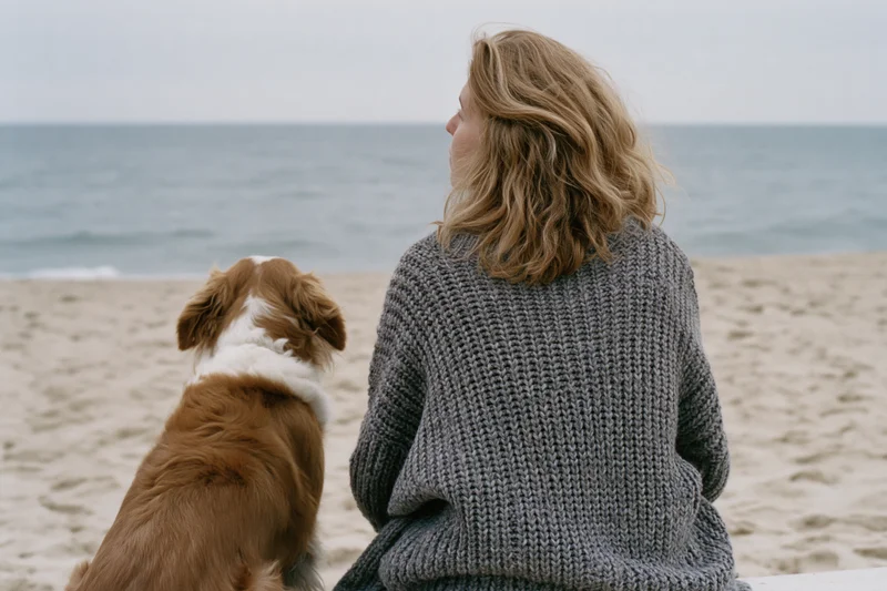 Woman and dog sitting on sandy beach facing ocean