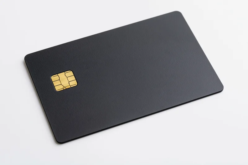 Matte black credit card with gold chip lying flat on white surface