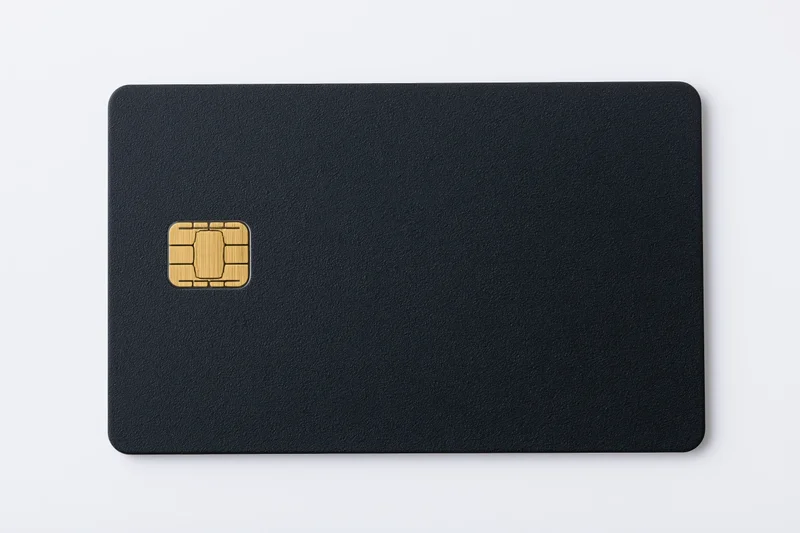 Matte black credit card with gold chip lying flat on white surface