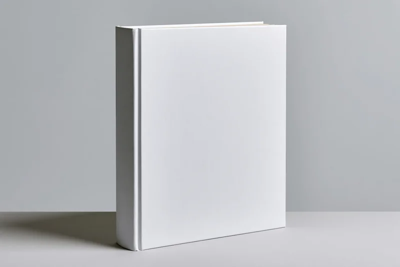 Blank white hardcover book standing upright on a gray surface with copyspace