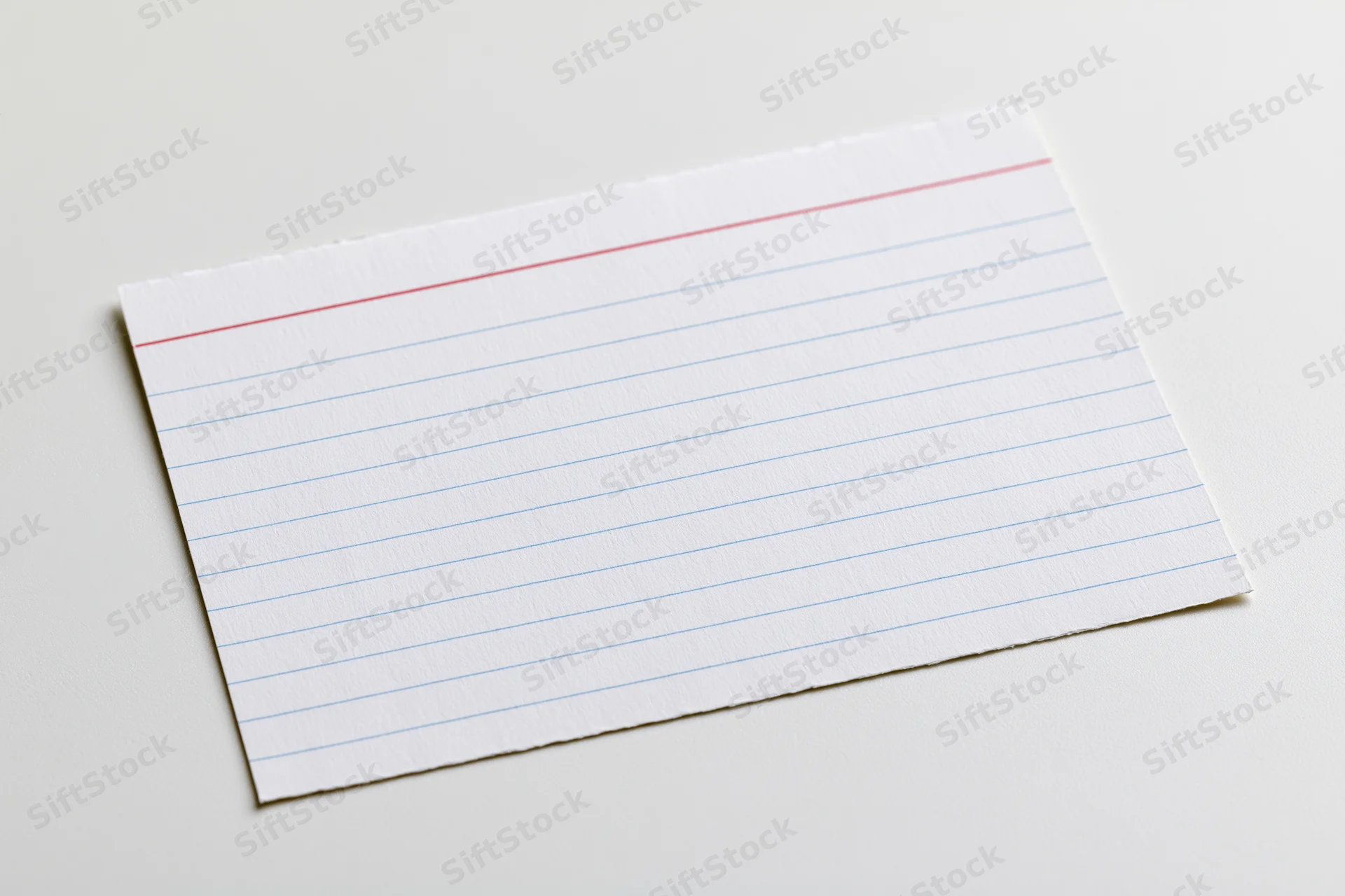 Blank ruled index card lying flat on white surface with torn edges and red margin line