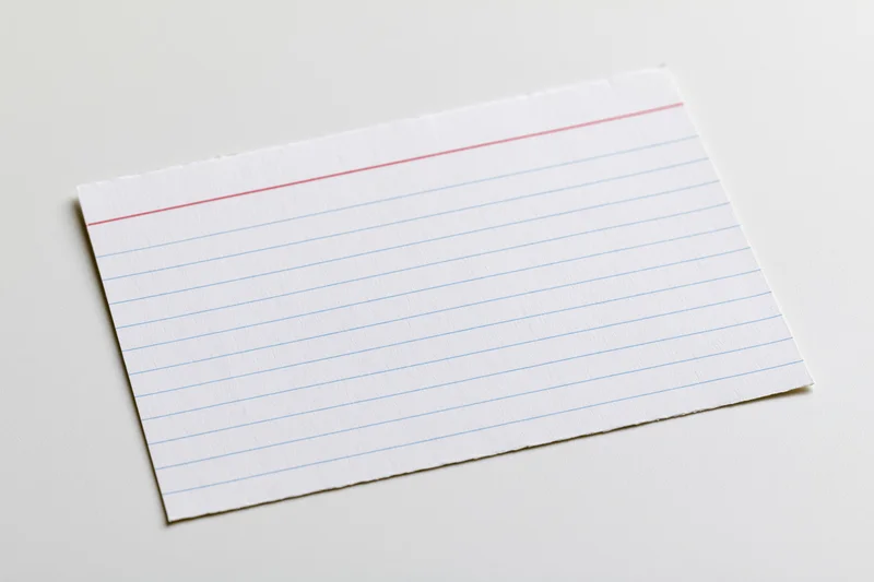 Blank ruled index card lying flat on white surface with torn edges and red margin line