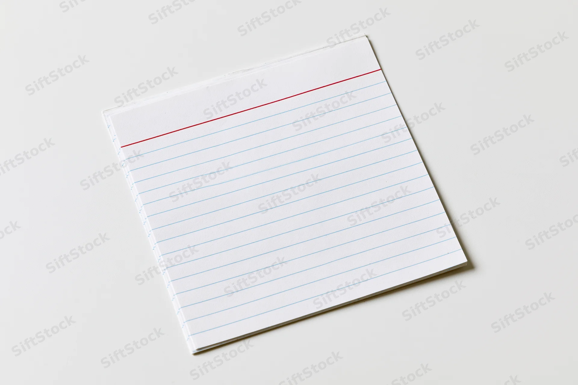 Blank lined notepad lying flat on white surface with copyspace