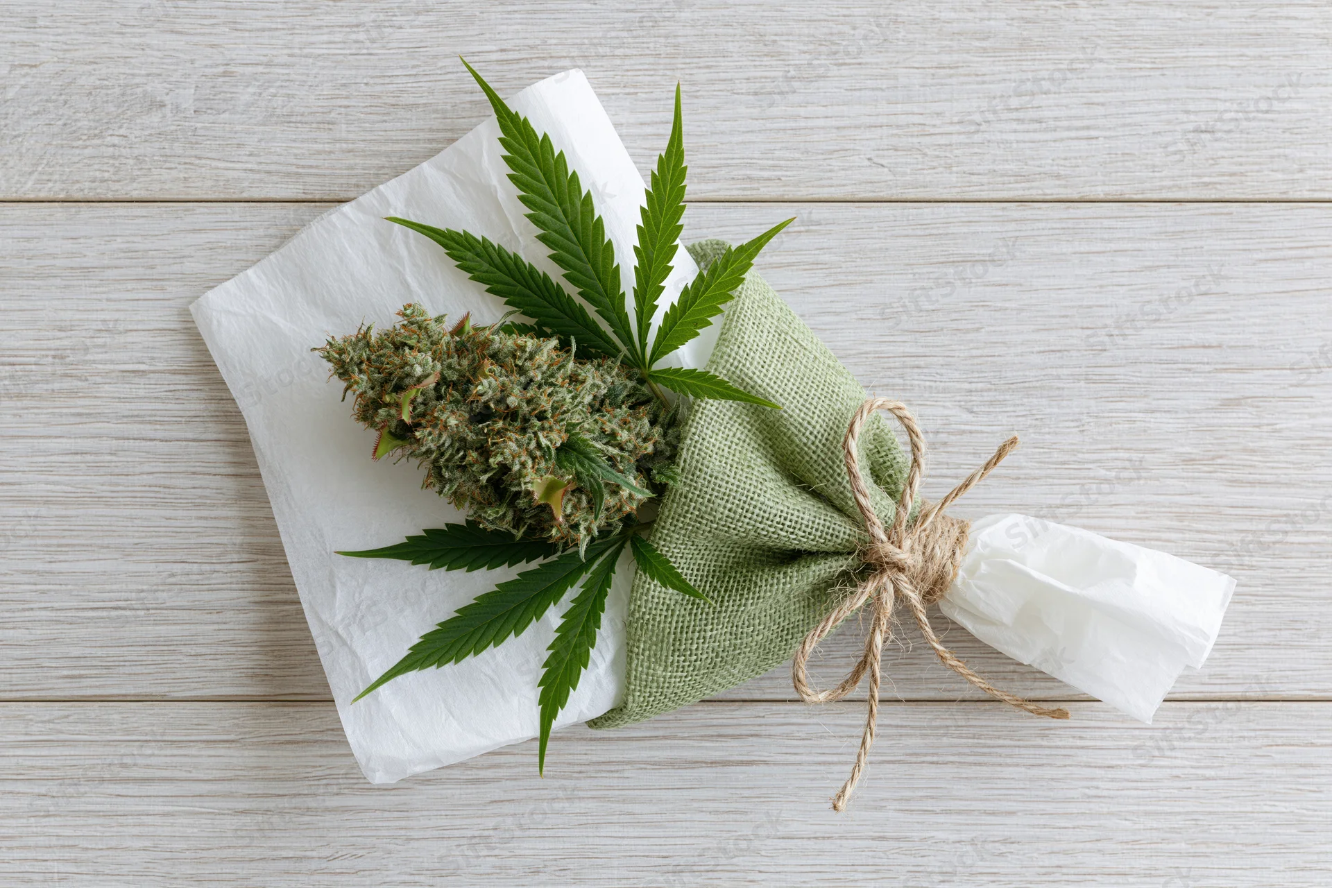 Cannabis bud wrapped as a gift bouquet with leaves and twine on a wooden surface