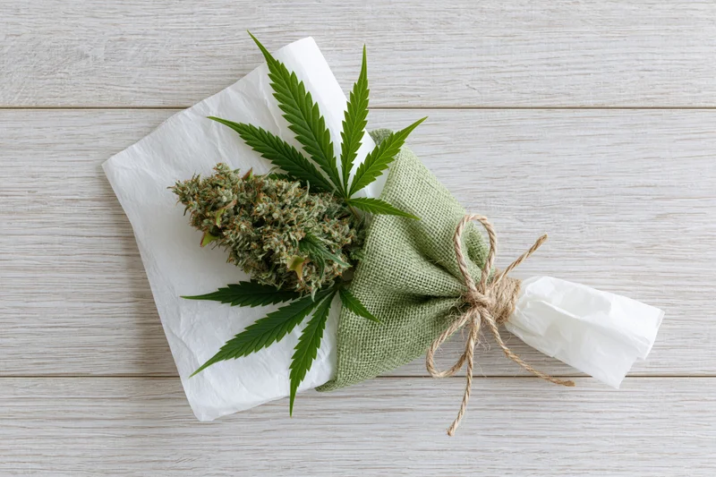 Cannabis bud wrapped as a gift bouquet with leaves and twine on a wooden surface