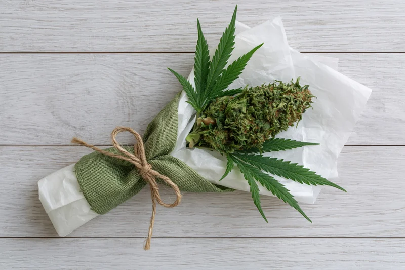 Cannabis bud wrapped as a gift bouquet with leaves on white wooden surface