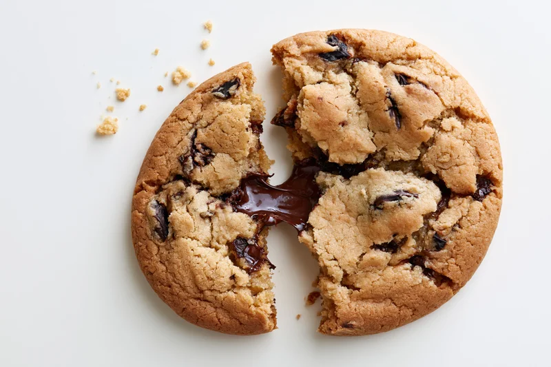 Chocolate chip cookie broken in half with melted chocolate oozing out on white surface