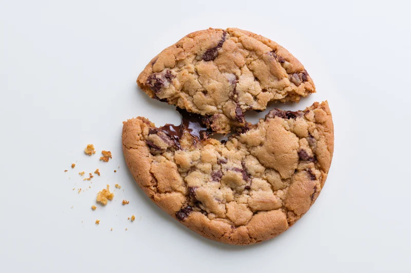 Broken chocolate chip cookie in half with melted chocolate on white background