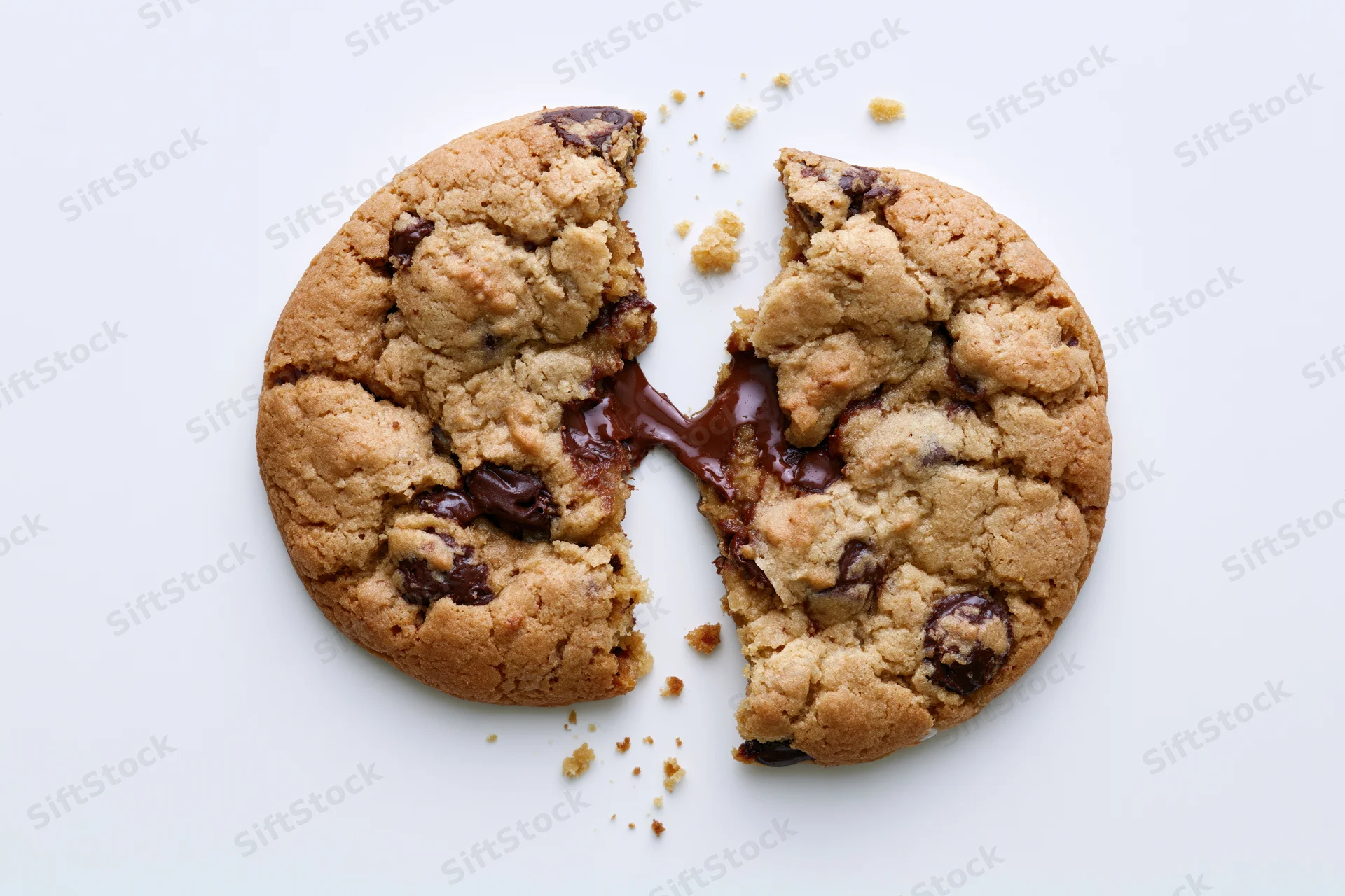 Chocolate chip cookie broken in half with melted chocolate oozing out on white surface