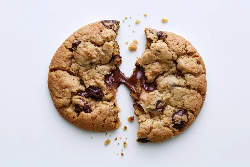 Chocolate chip cookie broken in half with melted chocolate oozing out on white surface