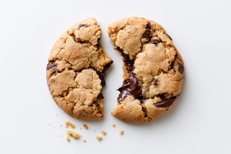 Chocolate chip cookie broken in half with melted chocolate and crumbs on white background