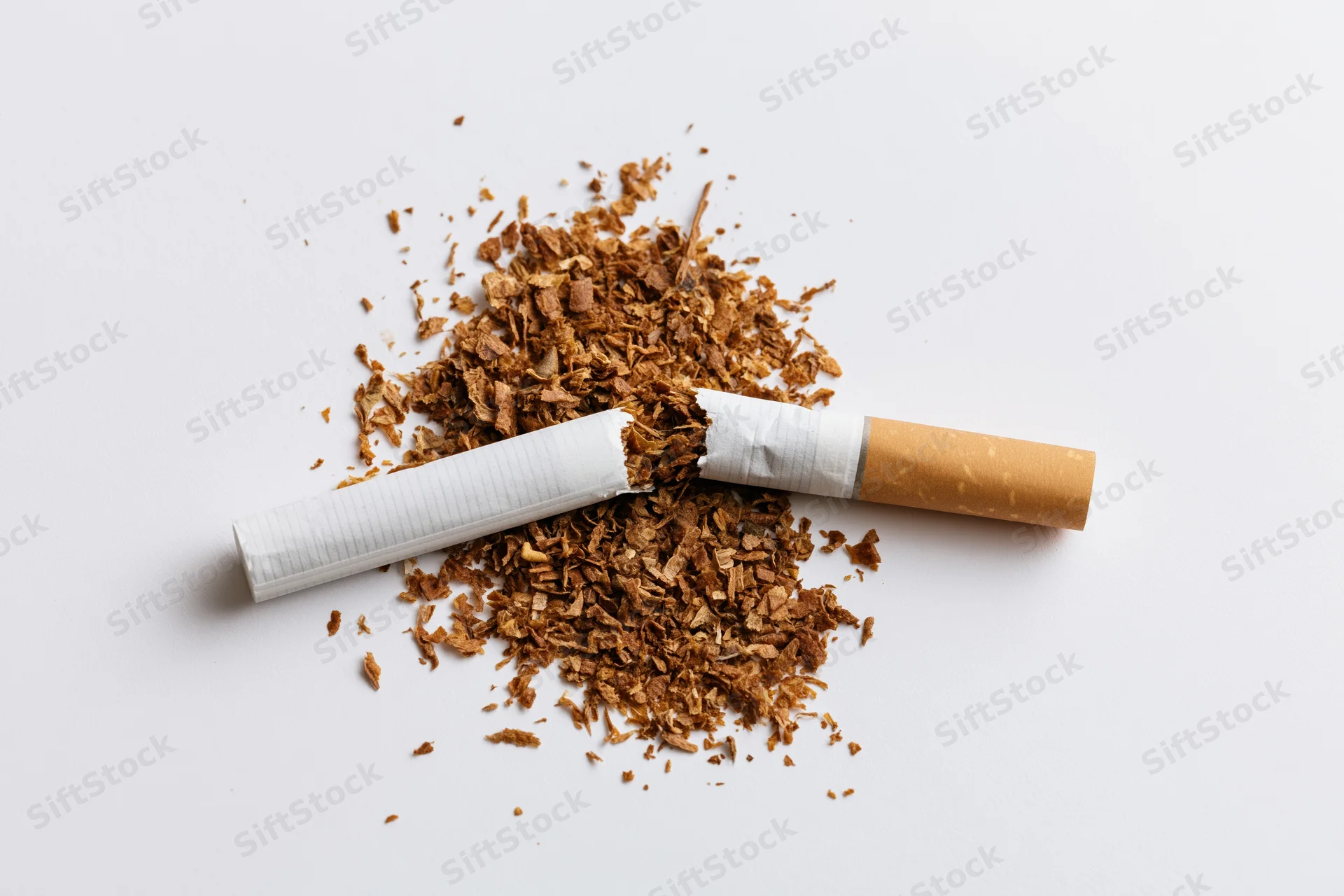 Broken cigarette snapped in half with loose brown tobacco on white background