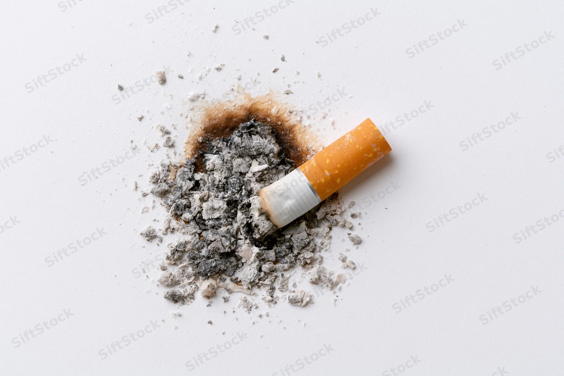 Cigarette stub with ash pile on plain white surface