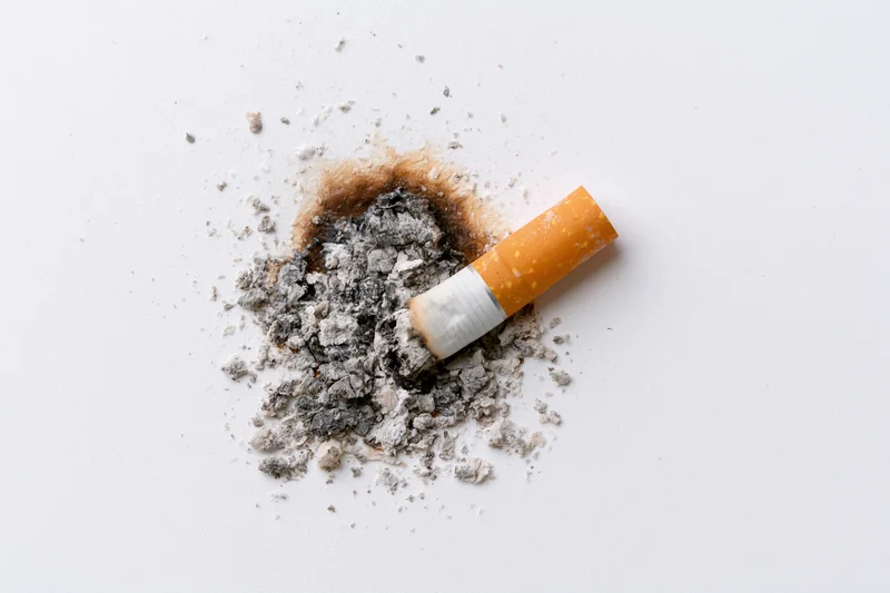 Cigarette stub with ash pile on plain white surface