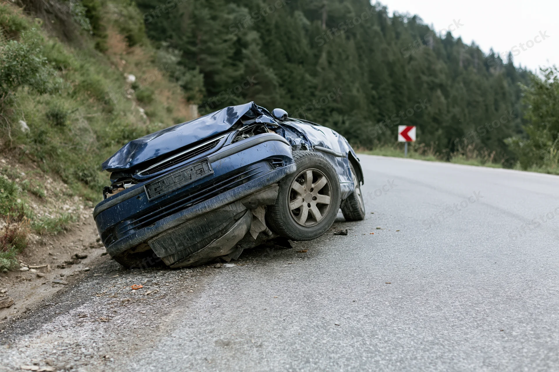 Dark blue sedan overturned on roadside shoulder near winding mountain road