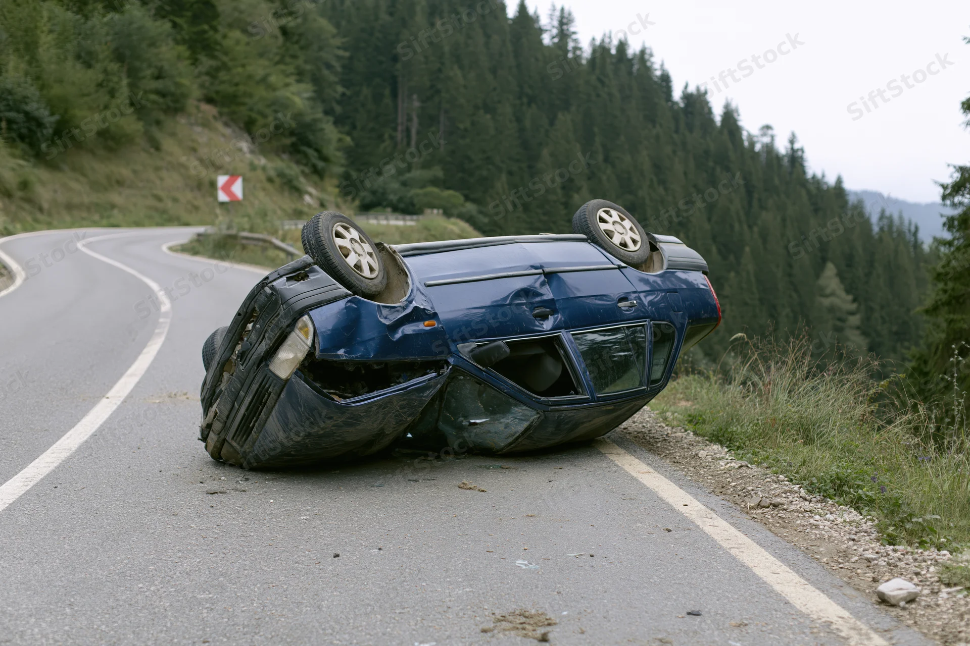 Dark blue sedan overturned on winding mountain road shoulder