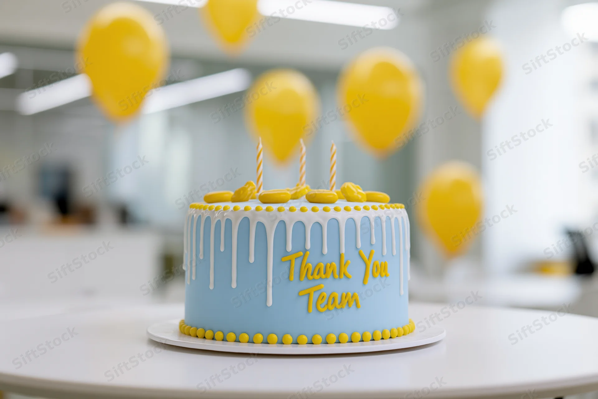Light blue fondant cake with white drizzle and yellow "thank you team" text on a table in an office with yellow balloons in the background
