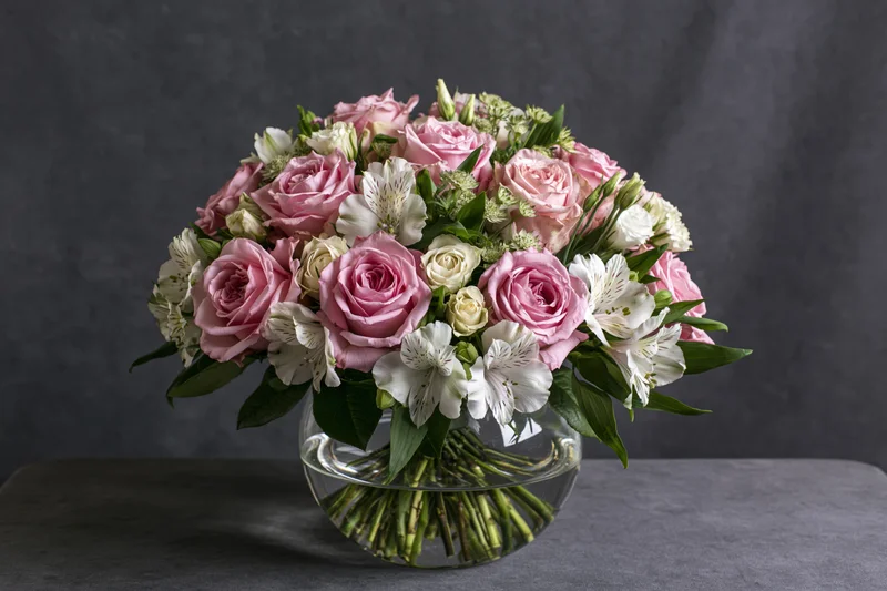 Pink roses and white alstroemeria arranged in a glass vase on a gray surface