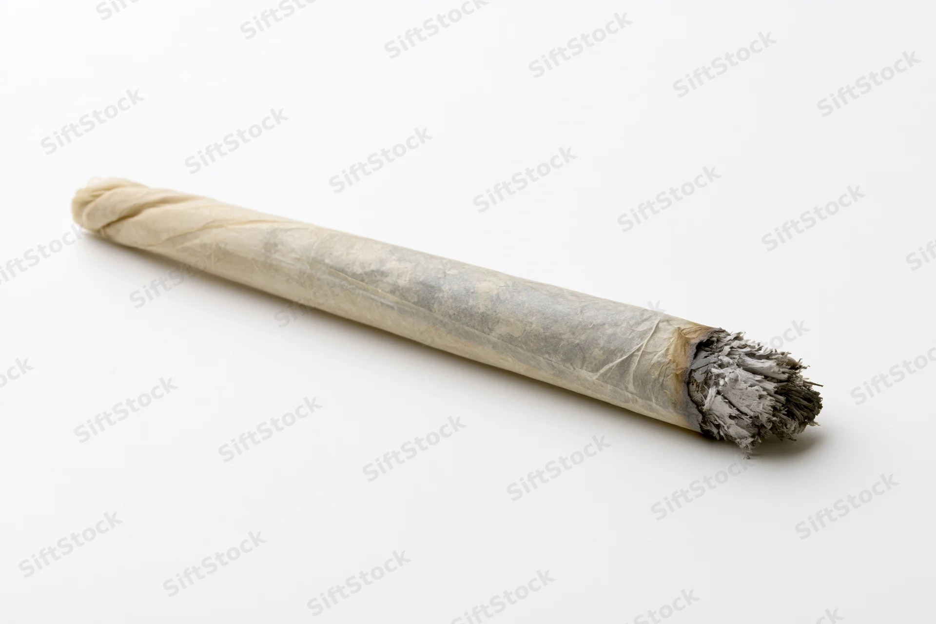 Hand-rolled cannabis joint with ash and twisted tip on white background