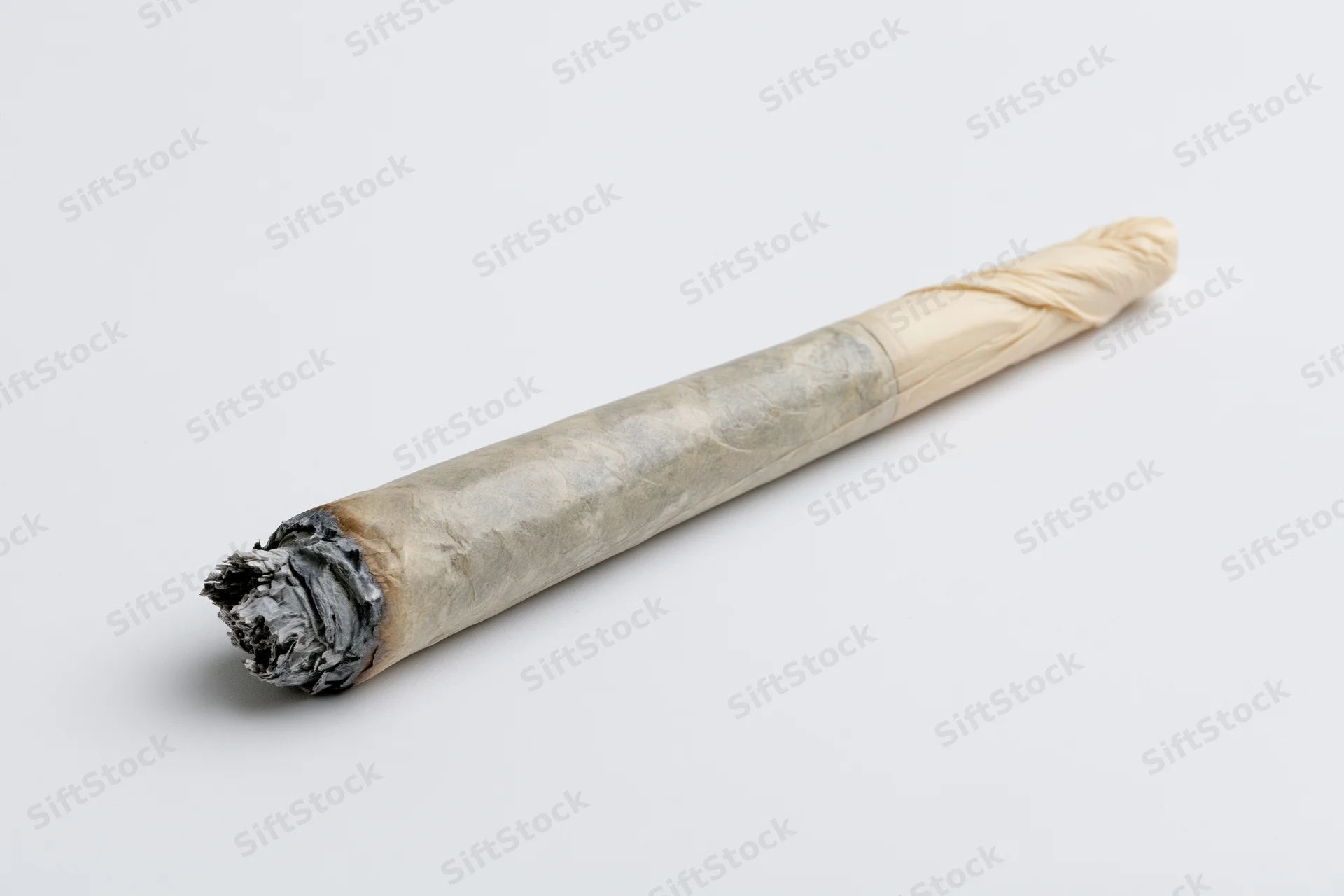 Hand-rolled cannabis joint with ash and twisted tip on plain white background