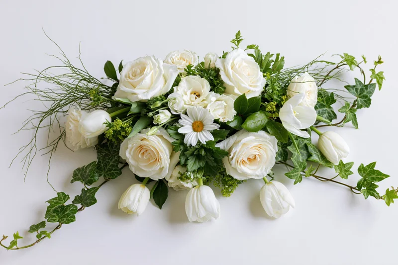 Horizontal floral arrangement of white roses and tulips with green ivy and daisies on white background