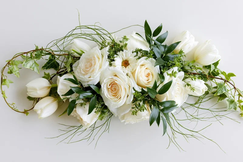 Horizontal floral arrangement of white roses and tulips with green foliage on white background
