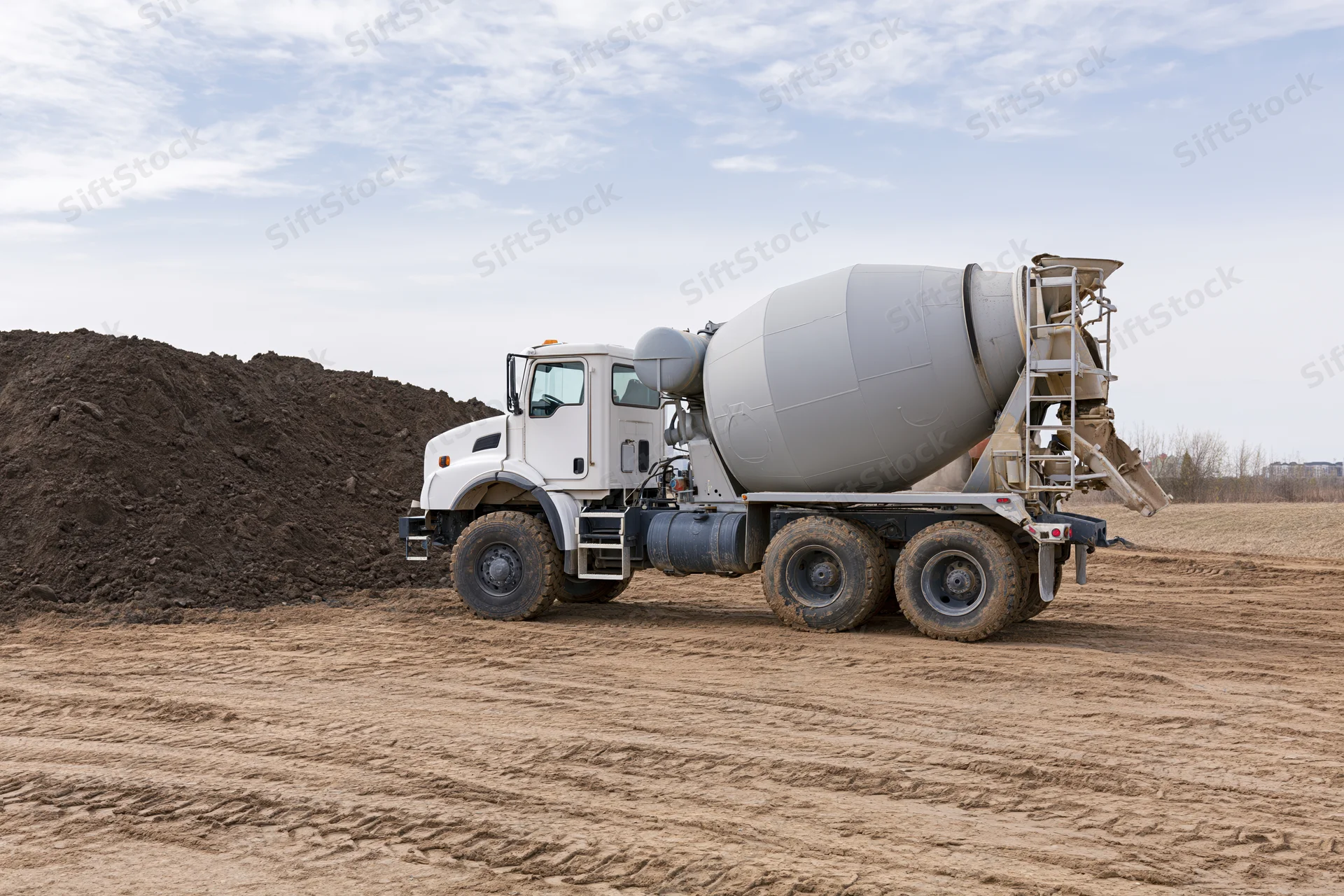 Cement mixer truck parked on a dirt construction site with a pile of soil nearby