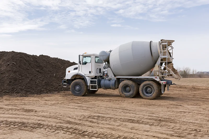 Cement mixer truck parked on a dirt construction site with a pile of soil nearby
