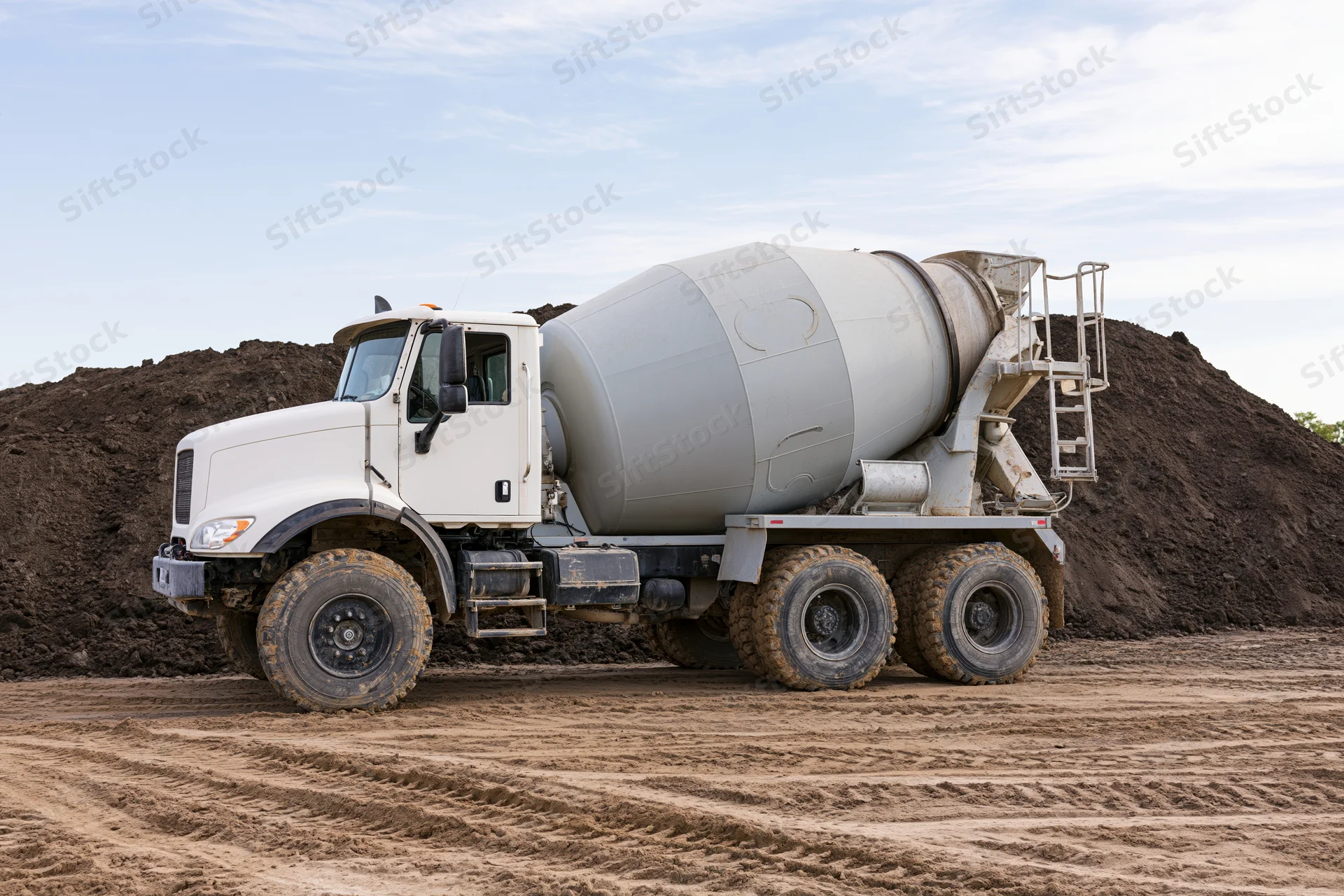 Cement mixer truck parked on a dirt construction site with soil piles in the background