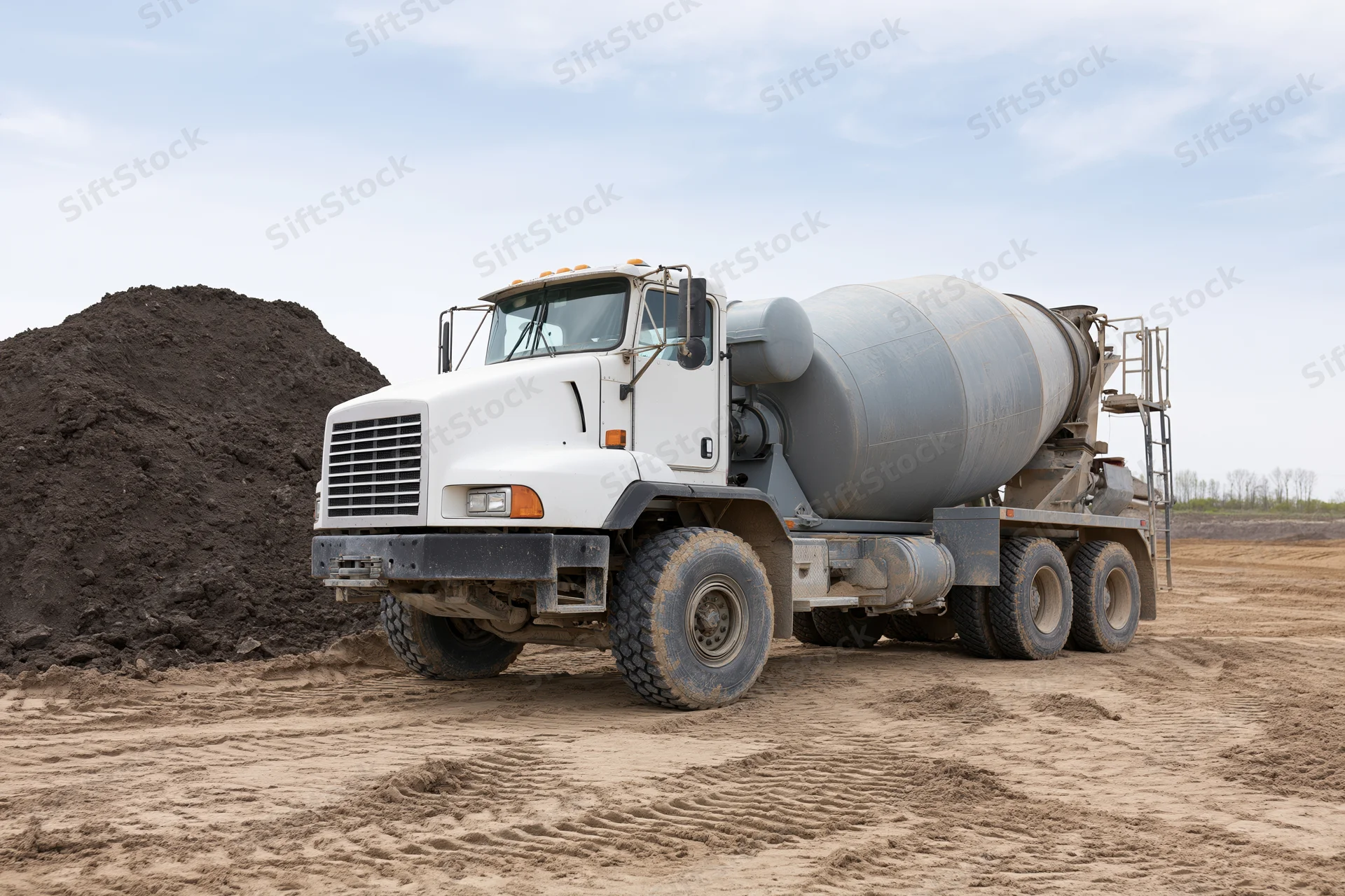 Cement mixer truck parked on a dirt construction site with a pile of soil nearby