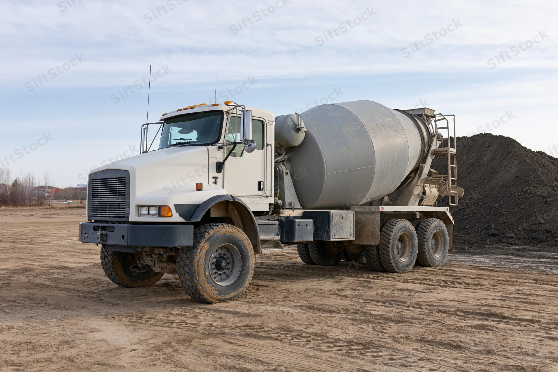 Cement mixer truck parked on a dirt construction site with gravel pile in background