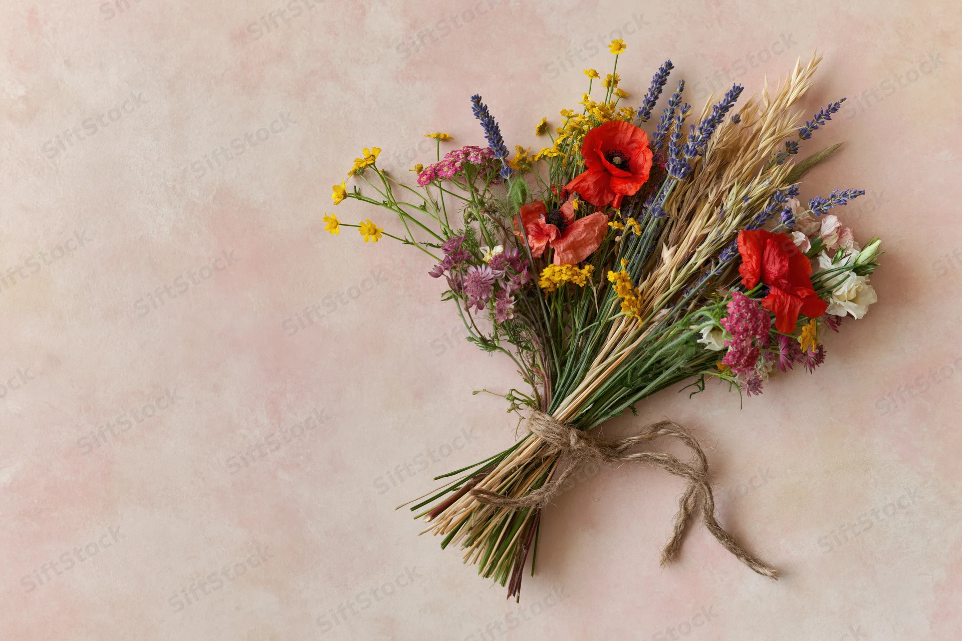 Loose wildflower bouquet tied with twine lying flat on pale blush pink surface