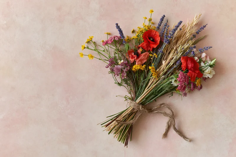 Loose wildflower bouquet tied with twine lying flat on pale blush pink surface